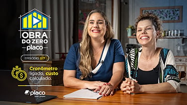 Duas mulheres sentadas à mesa sorrindo lado a lado.